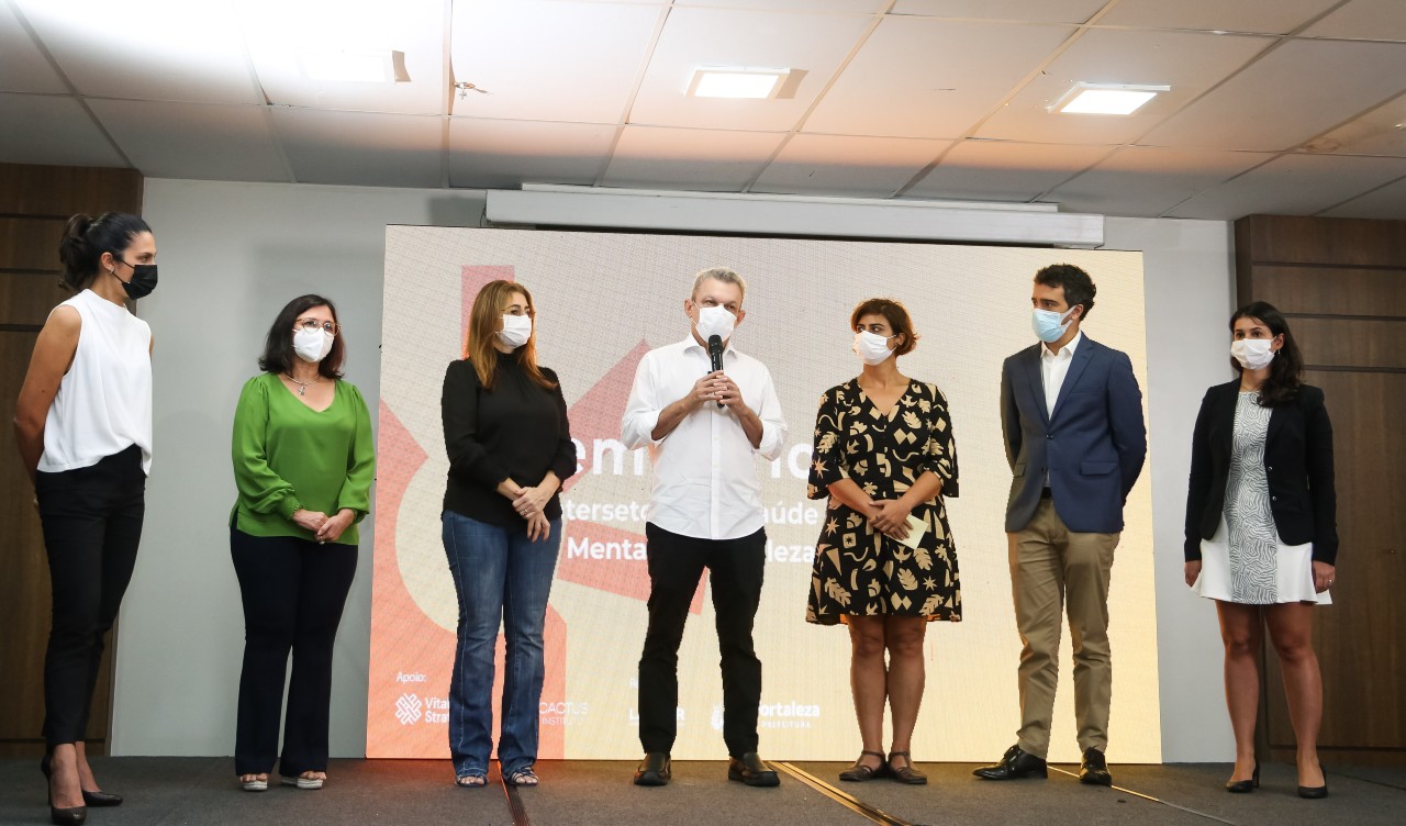 na foto, um grupo de pessoas está em pé num auditório 